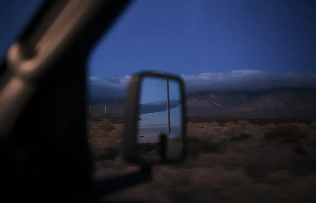 Looking out the passenger window of a motorhome at dusk with low shrubs in the foreground and with mountains in the far distance.