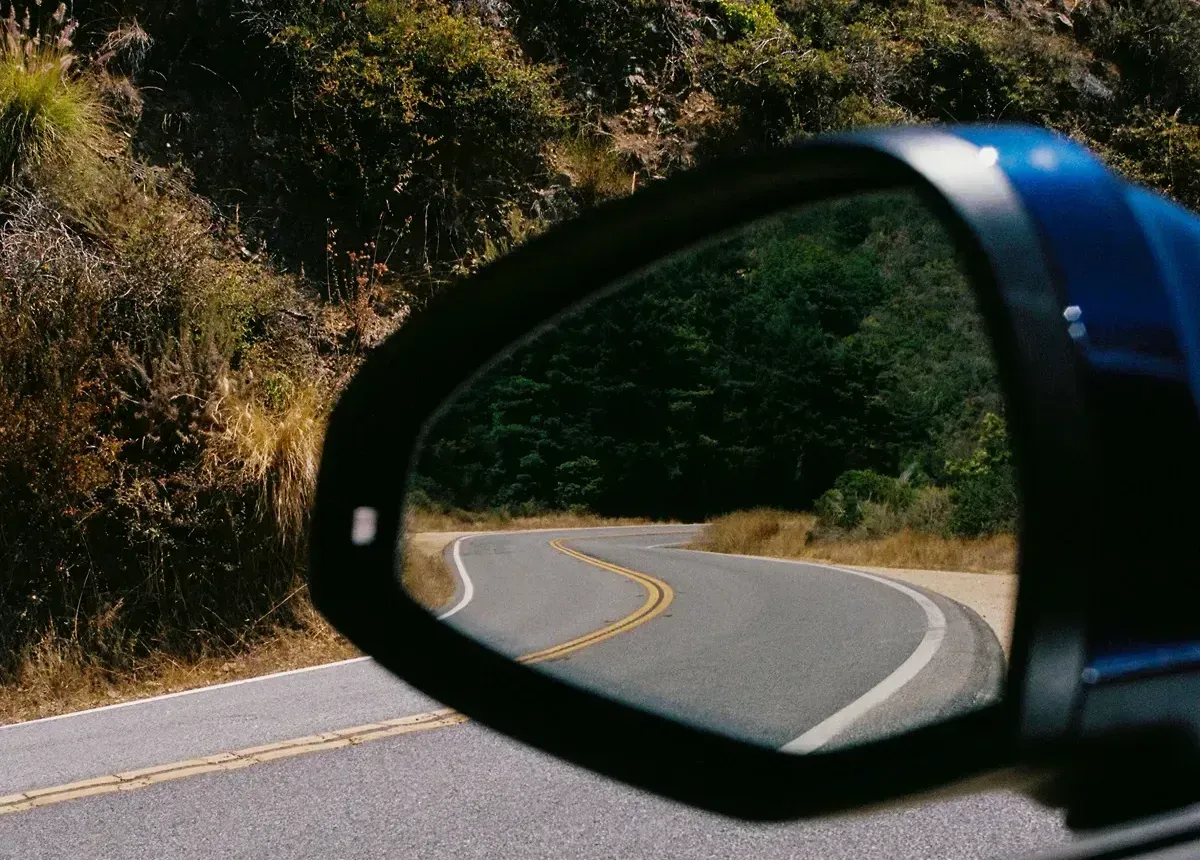 Driver side mirror showing a winding road