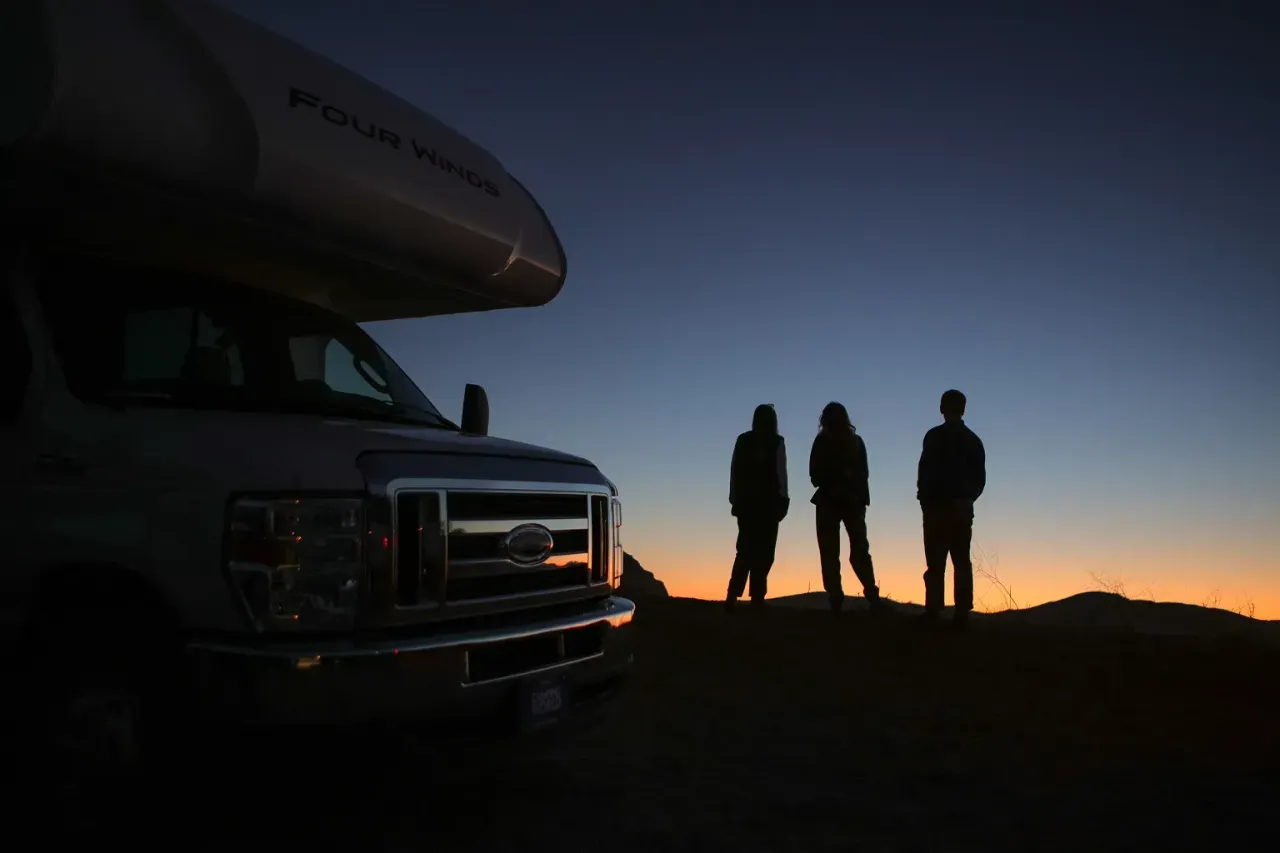 Three people watching the sunset on the side of the road near their motorhome.
