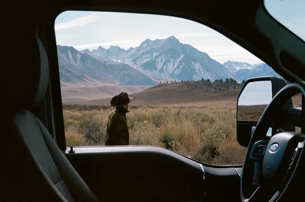Looking from the inside of an RV out the driver window at a man and a mountainous view