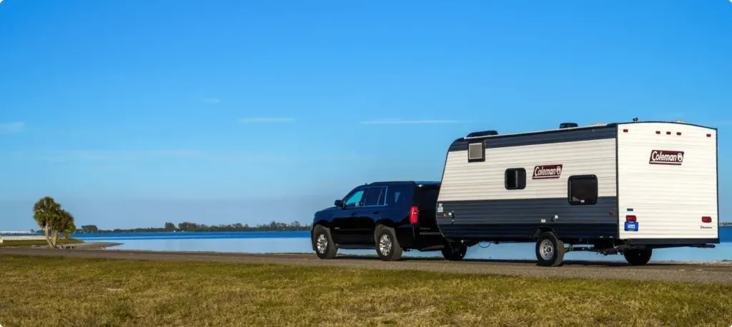An SUV pulls a trailer alongside a coastal waterway.
