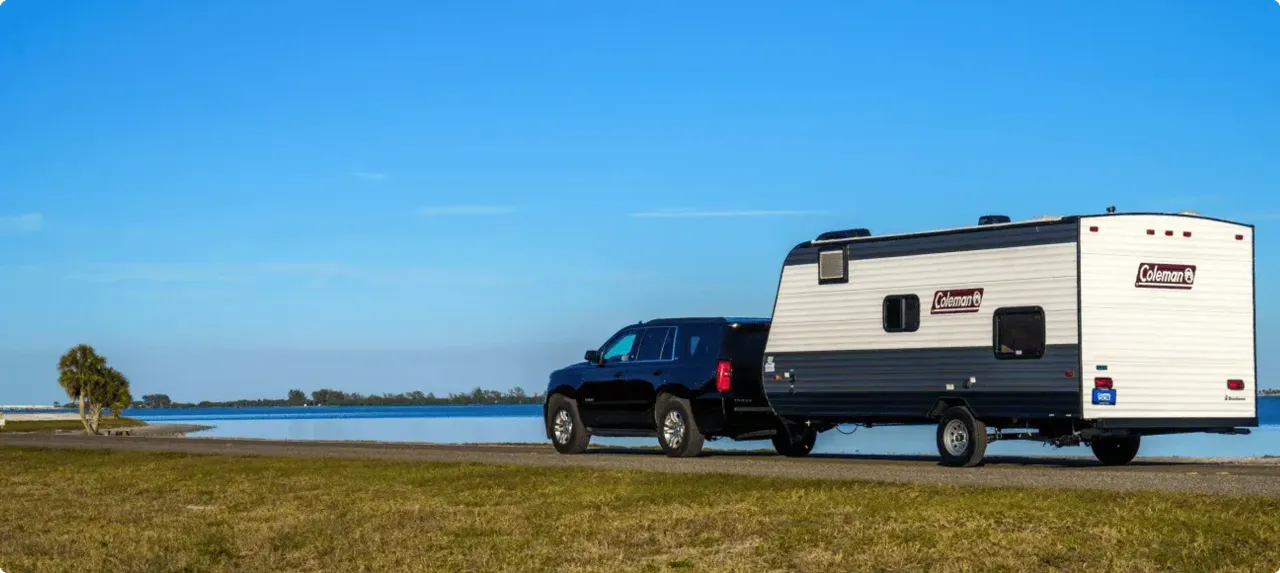 An SUV pulls a trailer alongside a coastal waterway.