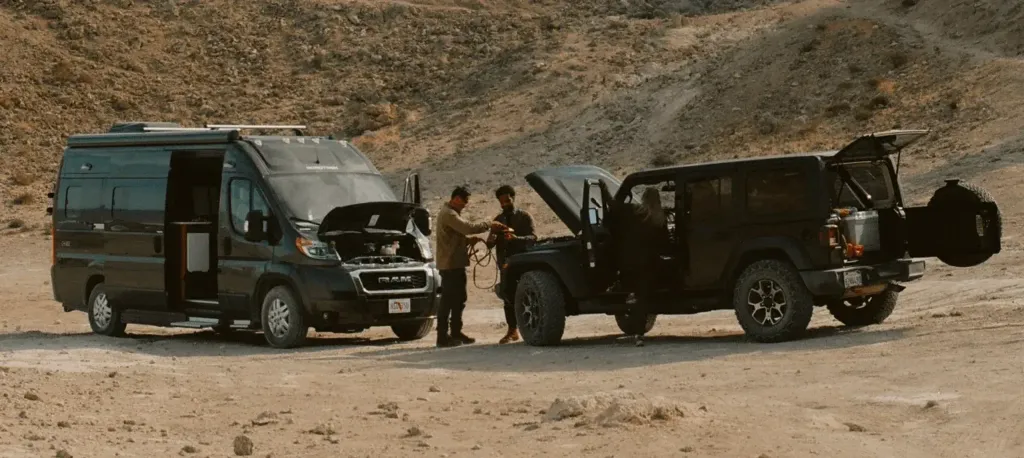Two men in the desert using an off-road SUV to jumpstart a Class B RV