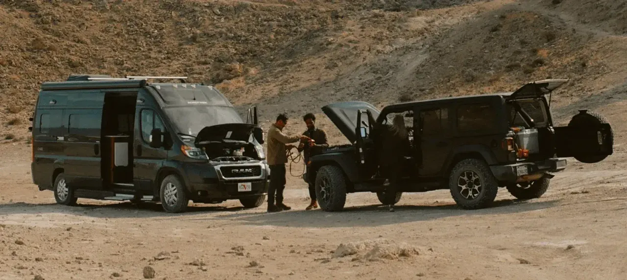 Two men in the desert using an off-road SUV to jumpstart a Class B RV