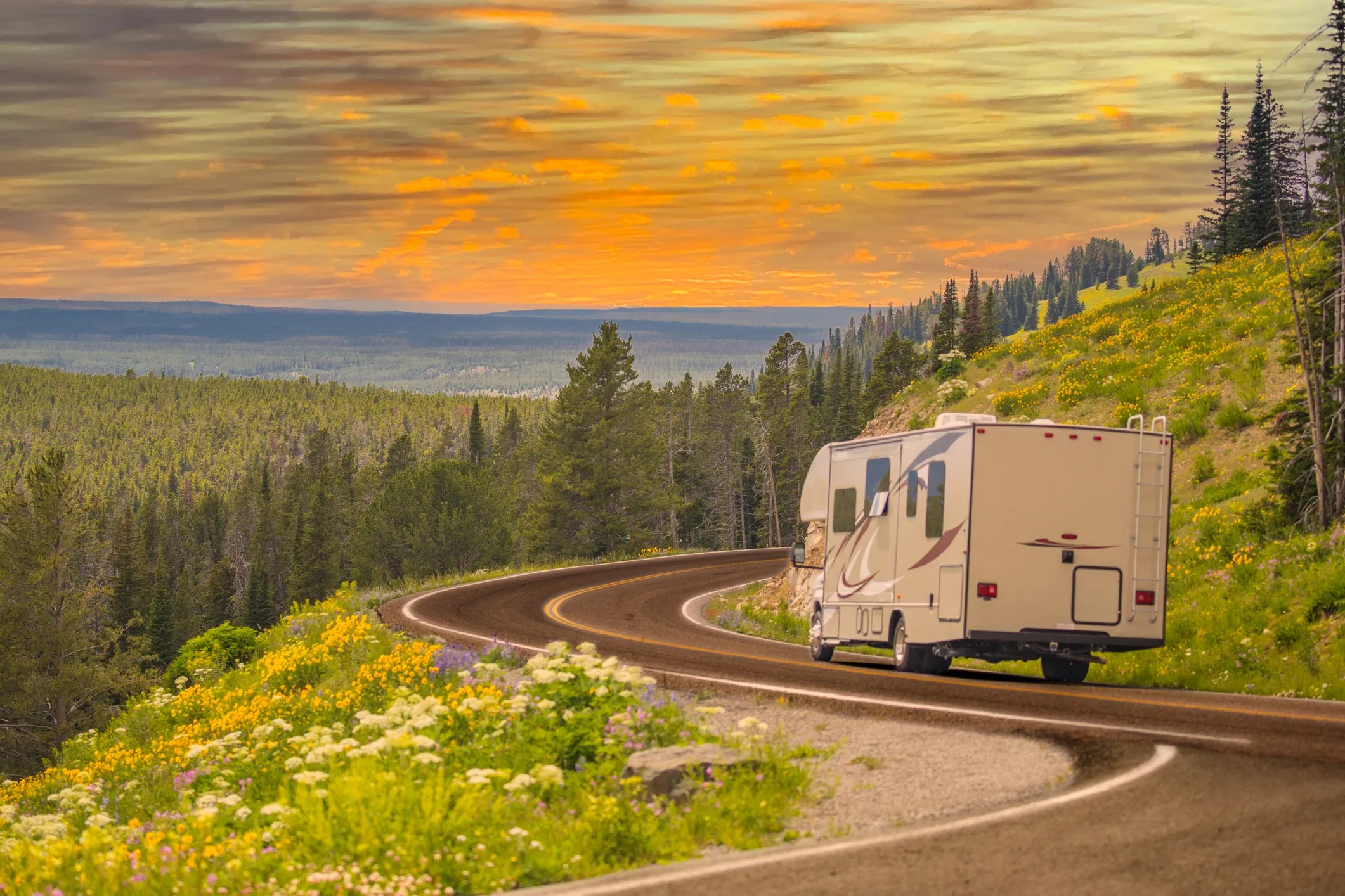 An RV driving on a winding road in the dusk with trees in the distance. 