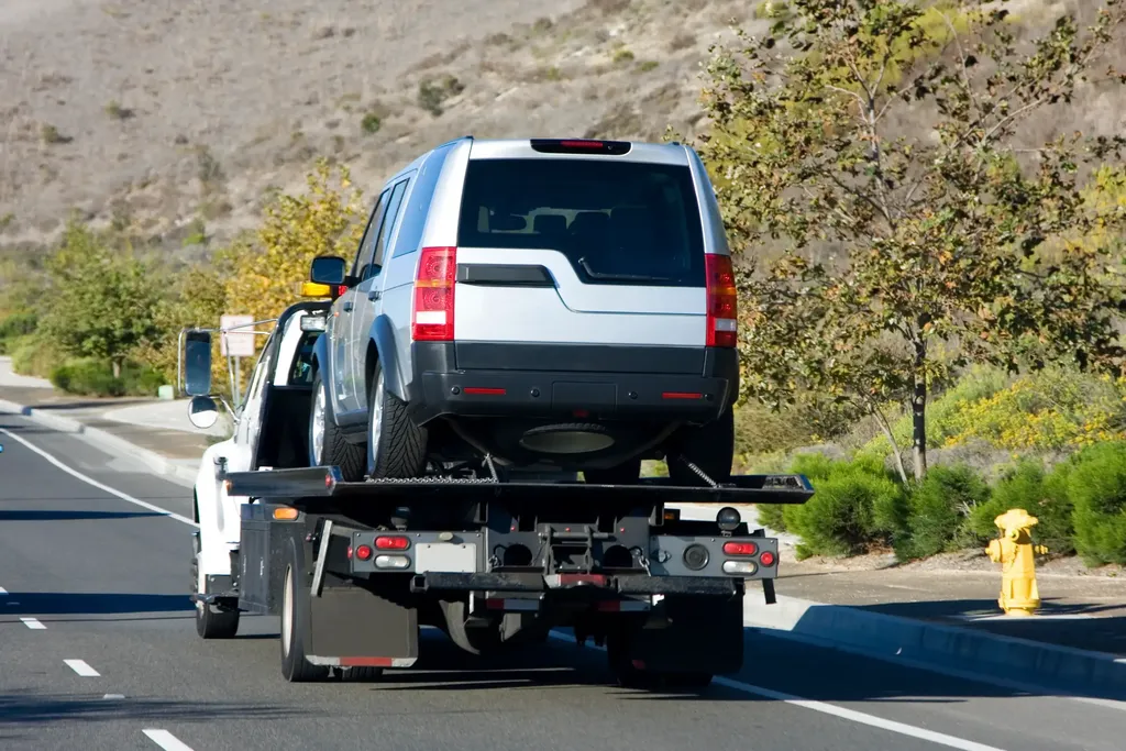 A silver SUV on a flat bed tow truck being towed. 