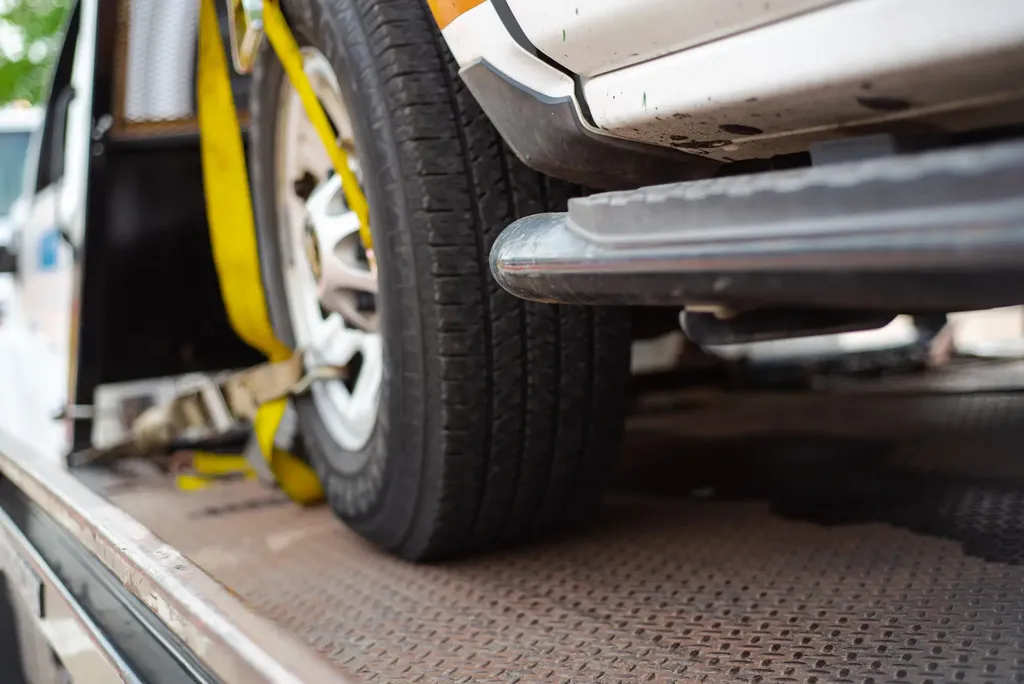 A closeup of a vehicle tire with a yellow strap attaching the vehicle to a flat tow truck.